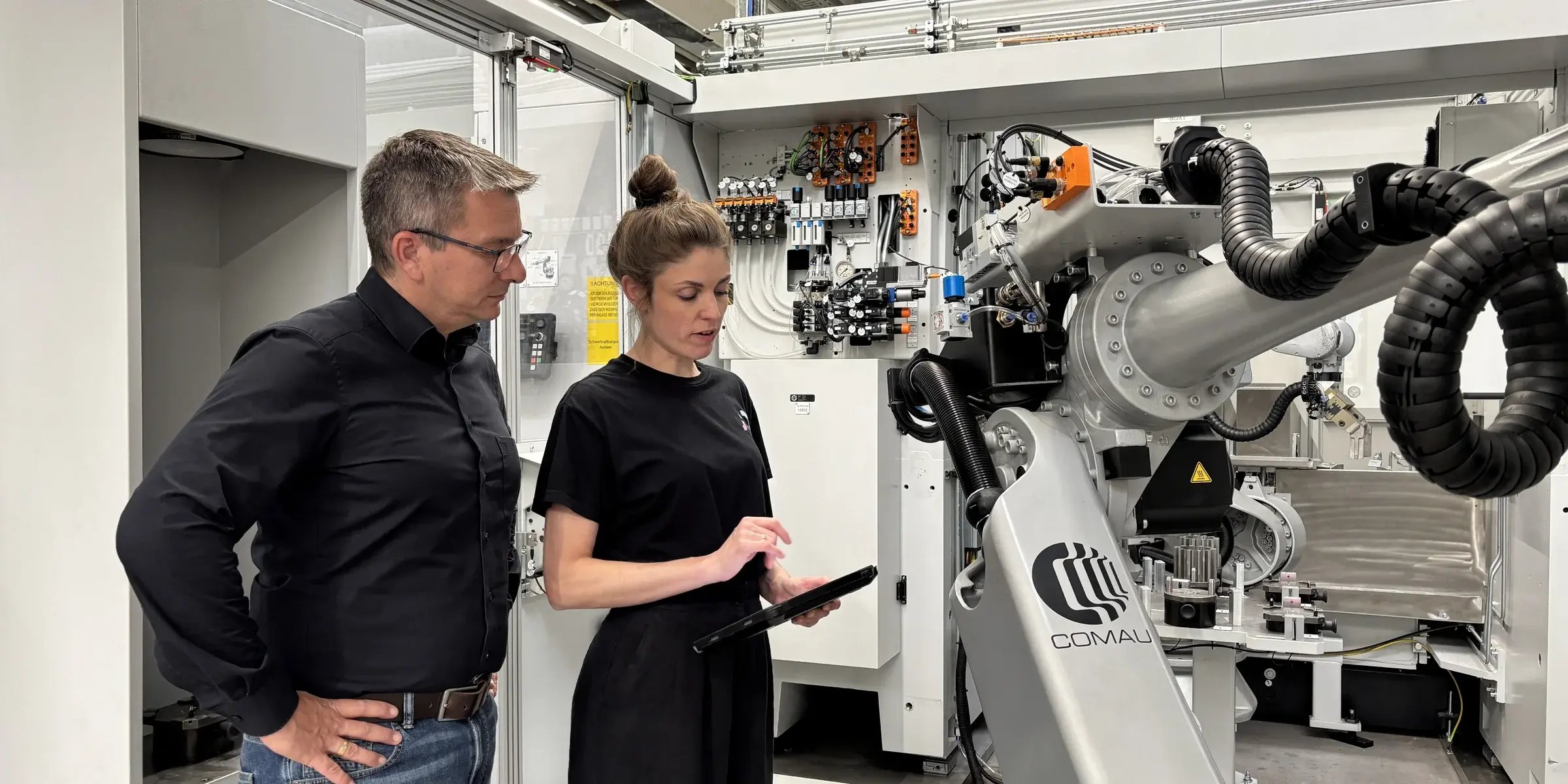 Sina Volkmann, CEO und Co-Founder von findIQ, und Peter Zech, Head of Innovation and Digitalization bei Siemens Bad Neustadt, stehen vor einer Maschine und schauen gemeinsam auf ein Tablet