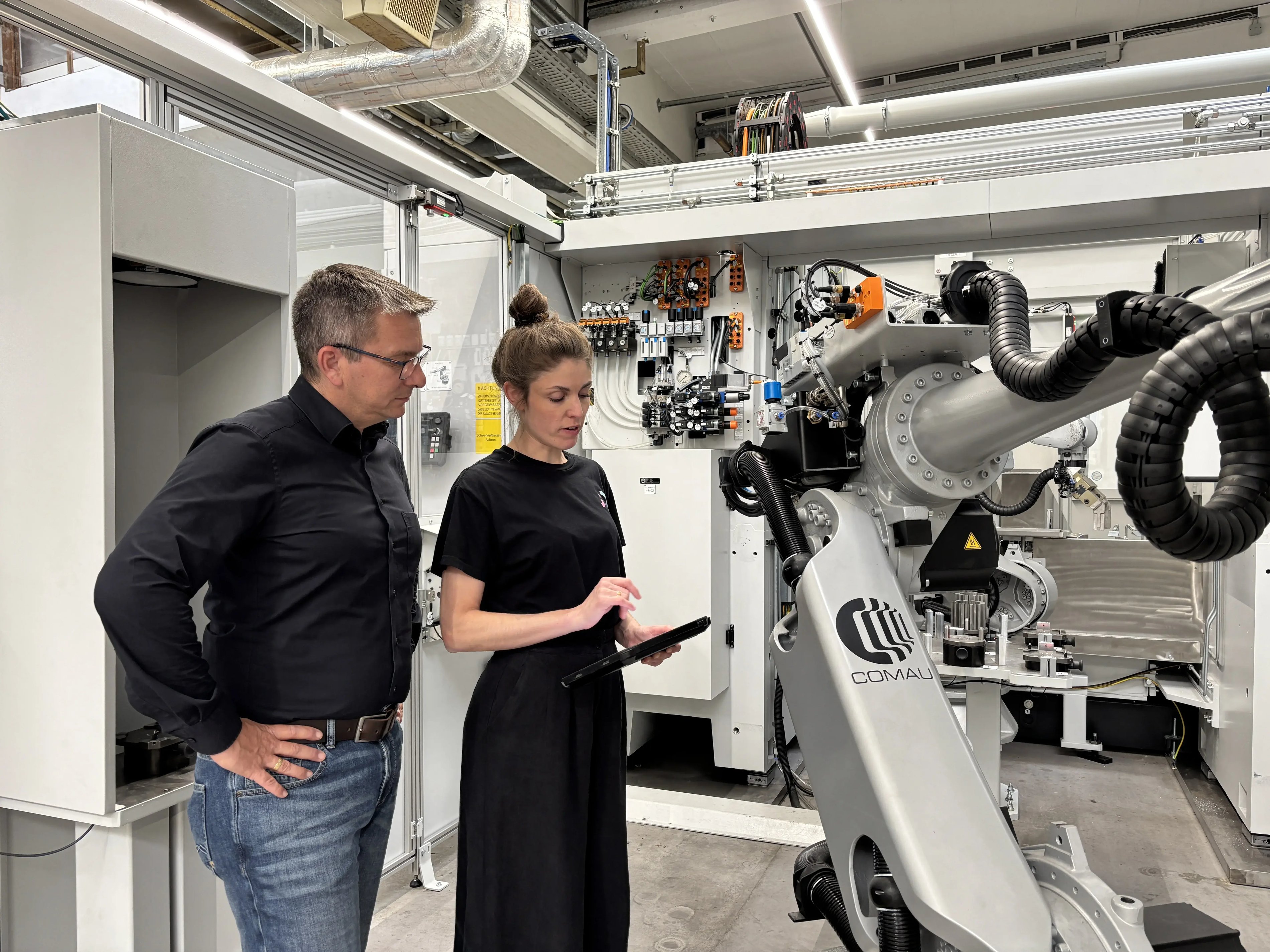 Sina Volkmann, CEO and Co-Founder of findIQ, and Peter Zech, Head of Innovation and Digitalization at Siemens Bad Neustadt, are standing in front of a machine and looking down at a tablet.