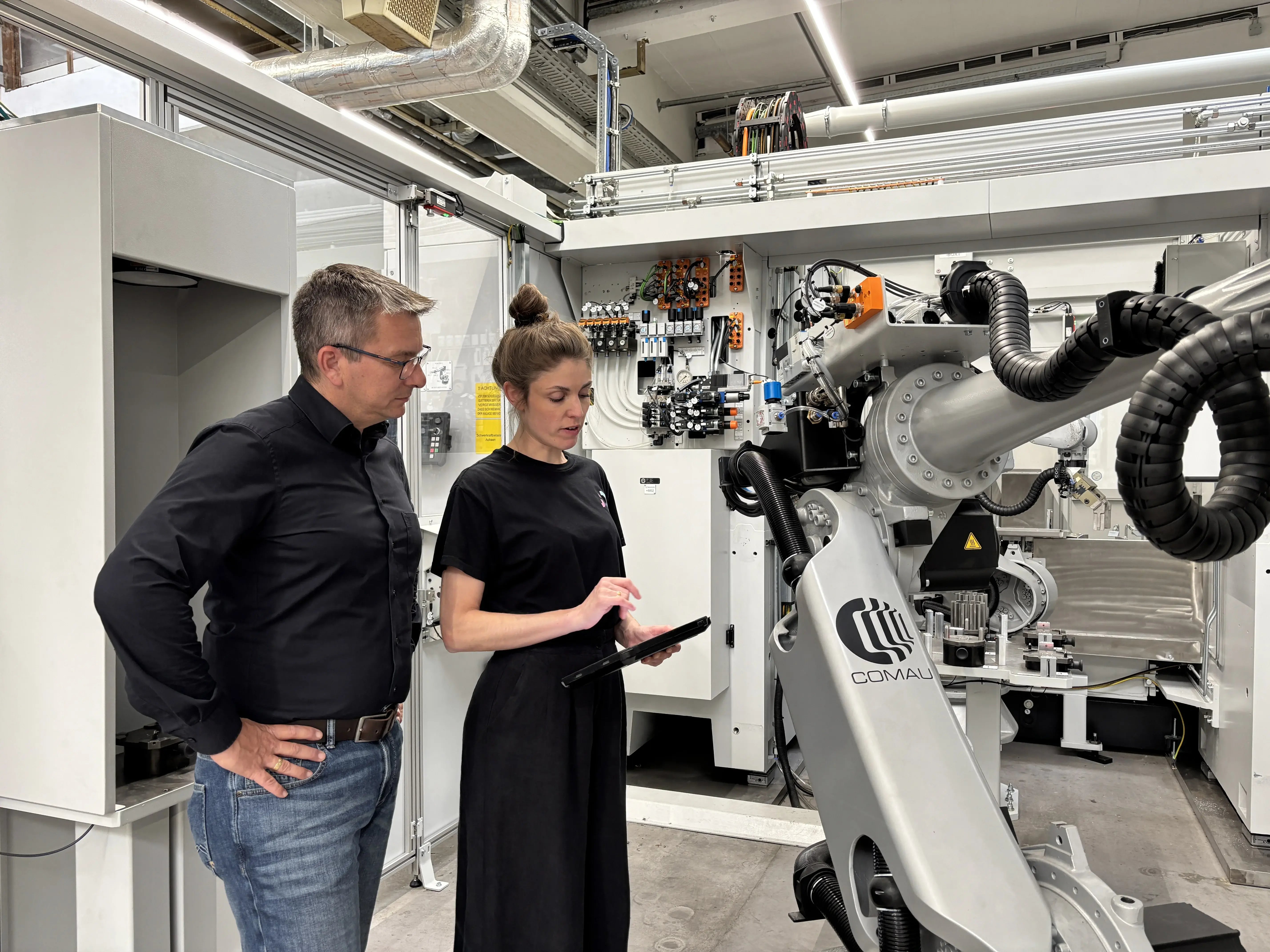 Sina Volkmann, CEO und Co-Founder von findIQ, und Peter Zech, Head of Innovation and Digitalization bei Siemens Bad Neustadt, stehen vor einer Maschine und schauen gemeinsam auf ein Tablet